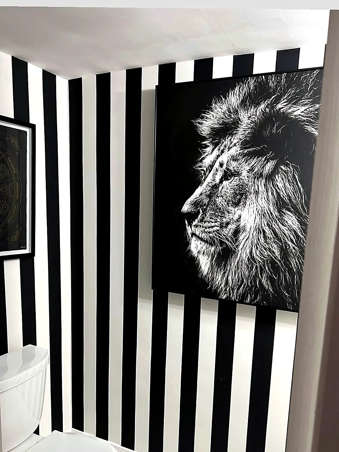 Black and white striped wallpaper with a lion canvas art piece installed in a powder room